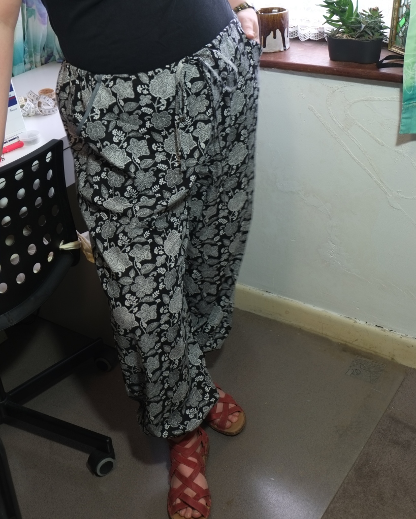 A woman is wearing black and white floral trousers with a plain black t-shirt. The trousers have slash pockets and are gathered at the ankles.