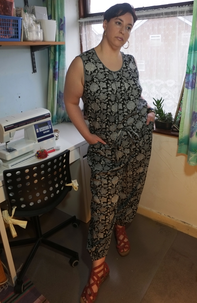 A woman is wearing a black and white floral print top and trousers. The top is sleeveless. The trousers have slash pockets and are gathered at the ankles.