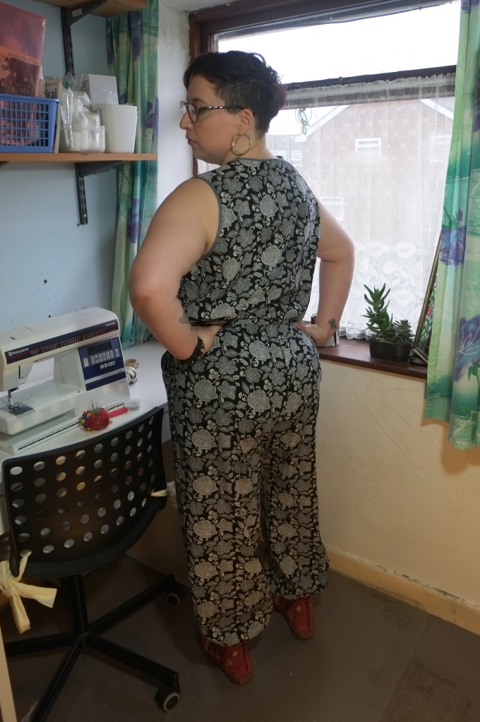 A woman is wearing a black and white floral print top and trousers. The top is sleeveless. The trousers have slash pockets and are gathered at the ankles.